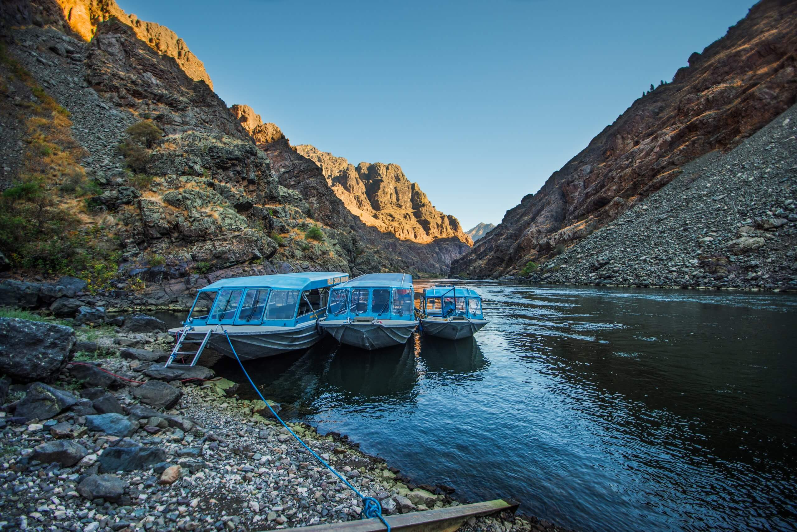 Three boats tied to the shores of a river in a canyon.