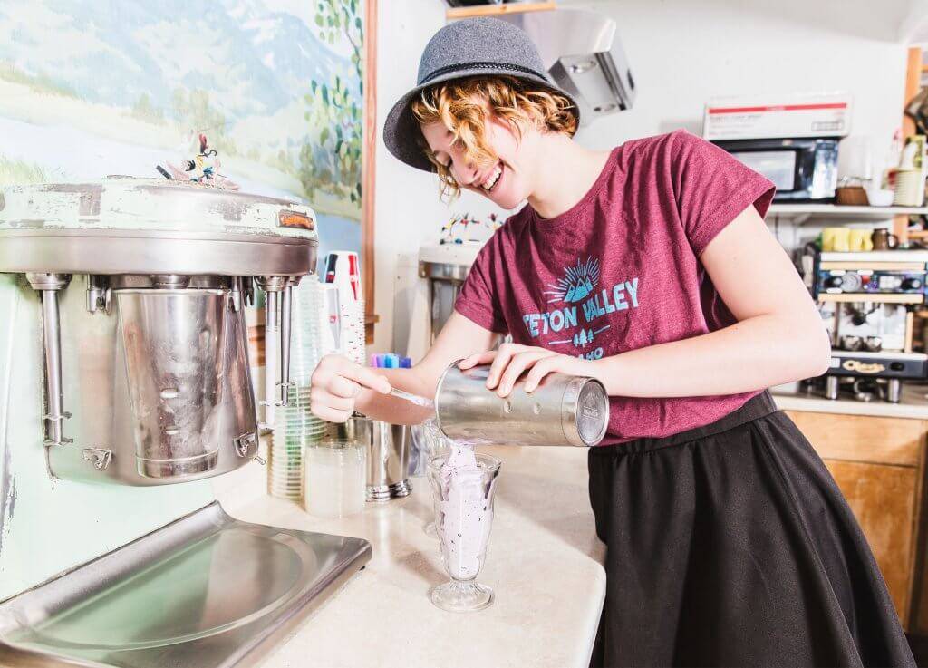 A woman pours a huckleberry milkshake into a glass at Victor Emporium.