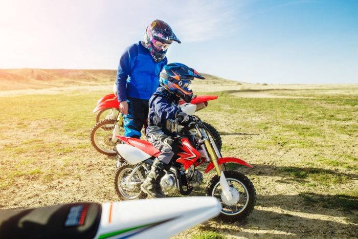 A father and son examining a dirt bike on a trail.