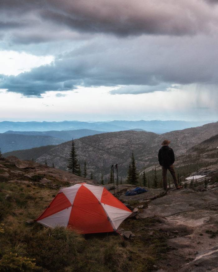Man standing by tent looking at the mountains.