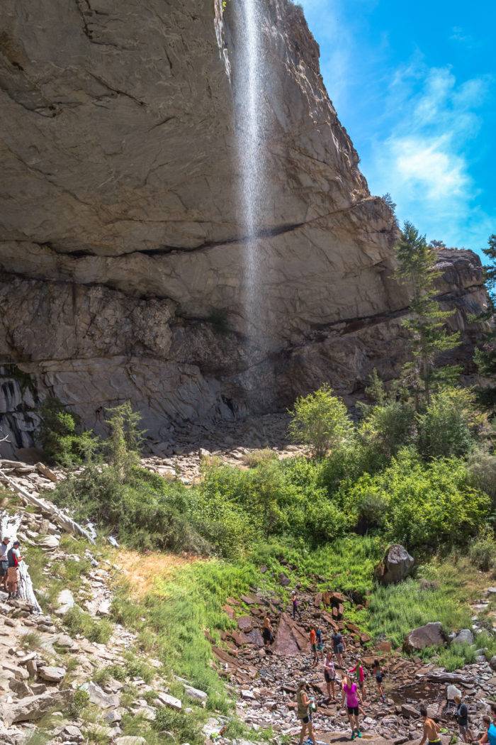 hikers below a waterfall falling off a cliffside