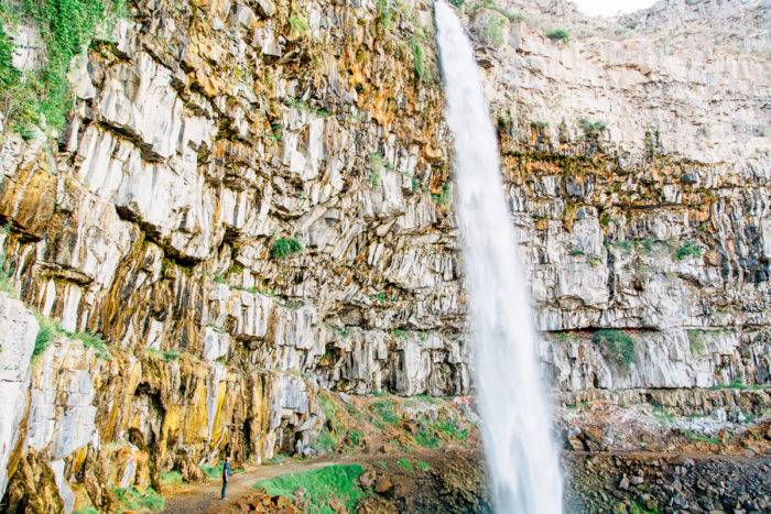 man standing near waterfall coming off of cliff edge