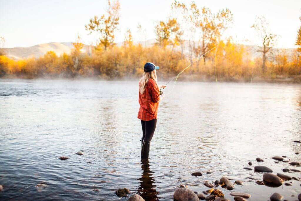 a woman in an orange plaid shirt fishing in the Boise River during fall.