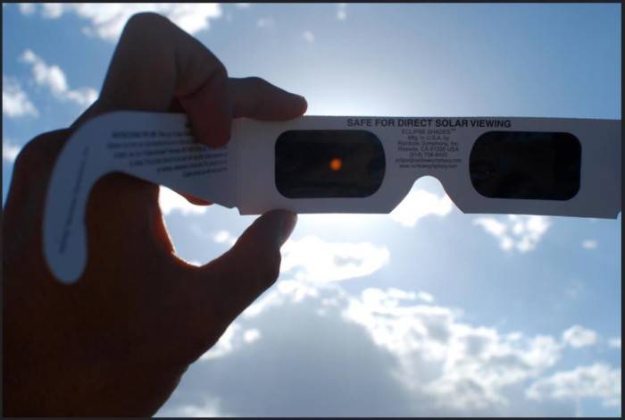 hand holding pair of eclipse glasses up to the sun.