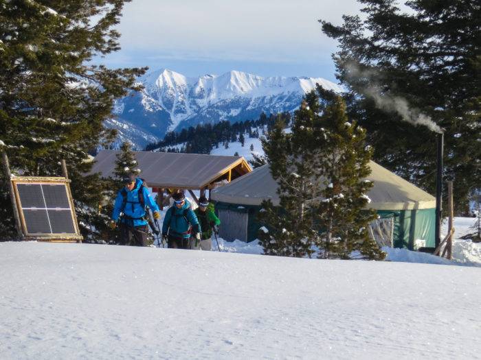 Three men leaving a yurt with a dramatic snow-capped mountain view in the background.