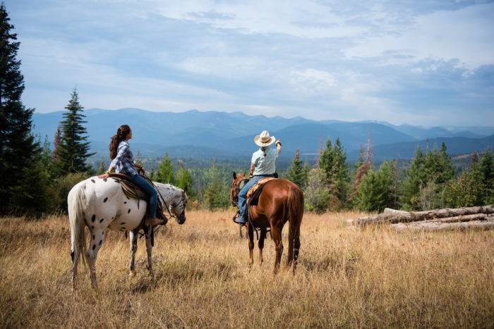 two women on horses looking over mountain valley