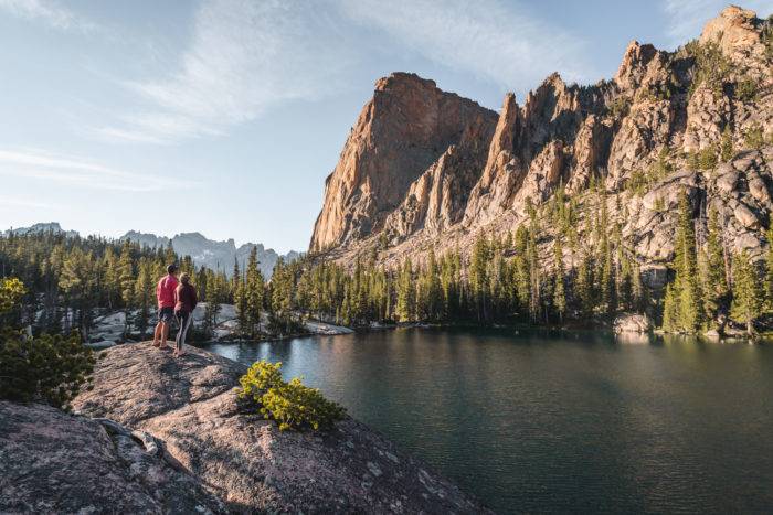Two people standing on a rock looking out over the Saddleback Lakes, trees and mountains.