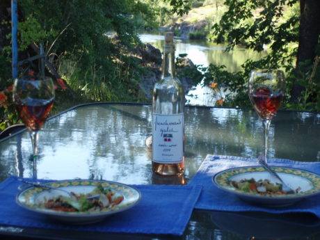 A table outsite along the river with dinner and a bottle of Frenchman's Gulch wine.
