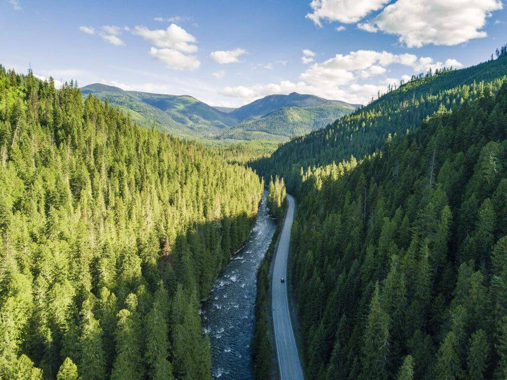 Aerial shot of a car driving along Highway 12 near Kooskia with a map of Idaho that features an outline of the north central region overlaid. 