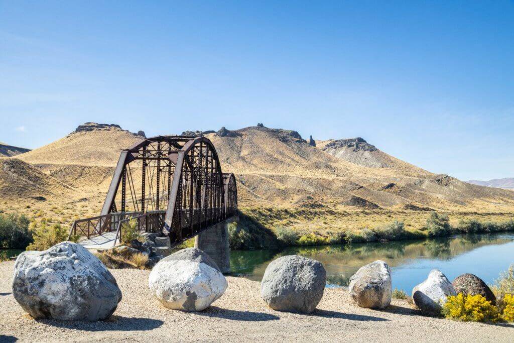 a railroad bridge spanning across a river with mountains in the background