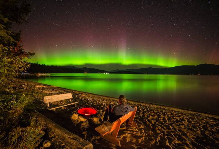 man sitting on beach watching northern lights at Hill's Resort