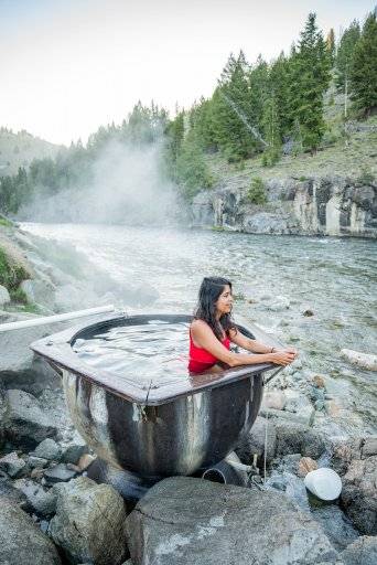 a woman sitting in a hot spring next to a river