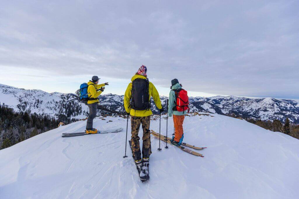 three skiers at top of peak assessing ski area