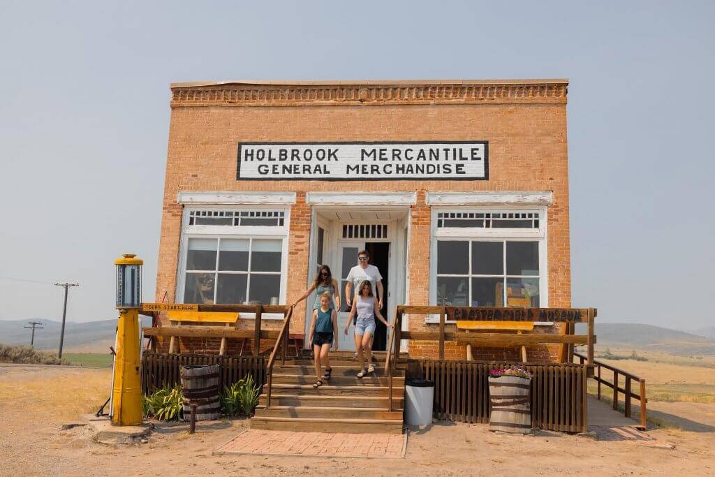 A family of four walking out of a brick building with a sign that reads "Holbrook Mercantile General Merchandise" in Chesterfield Historic Town Site.