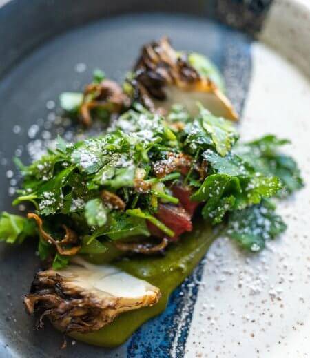 dark plate with Skirt steak, maitake, spinach, chimichurri, lemon, herbs.