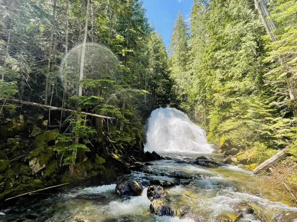 Snow Creek Falls tumbles over large, rocky edge surrounded by tall trees and other forestation