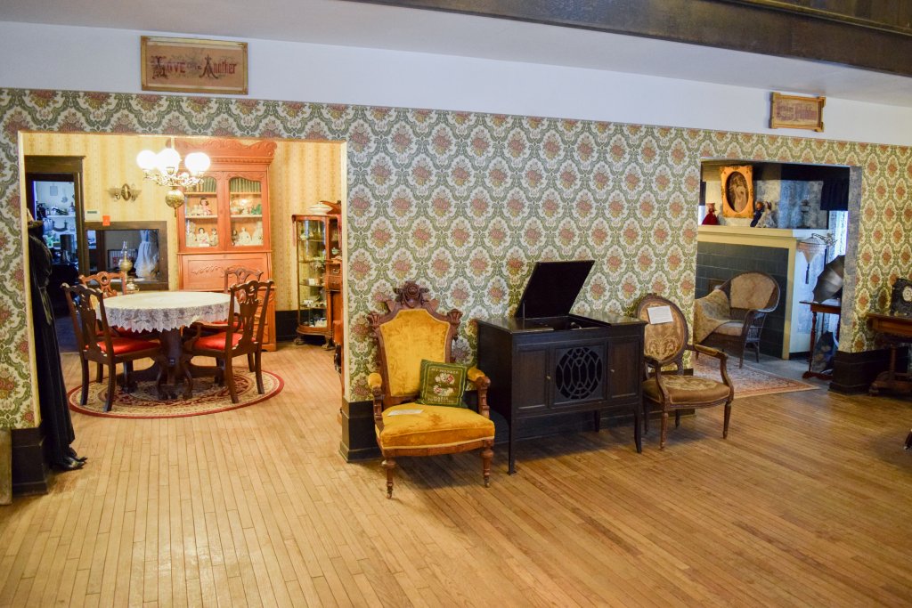 Two rooms containing antique tables, chairs and other furniture inside the Bingham County Historical Society Museum.