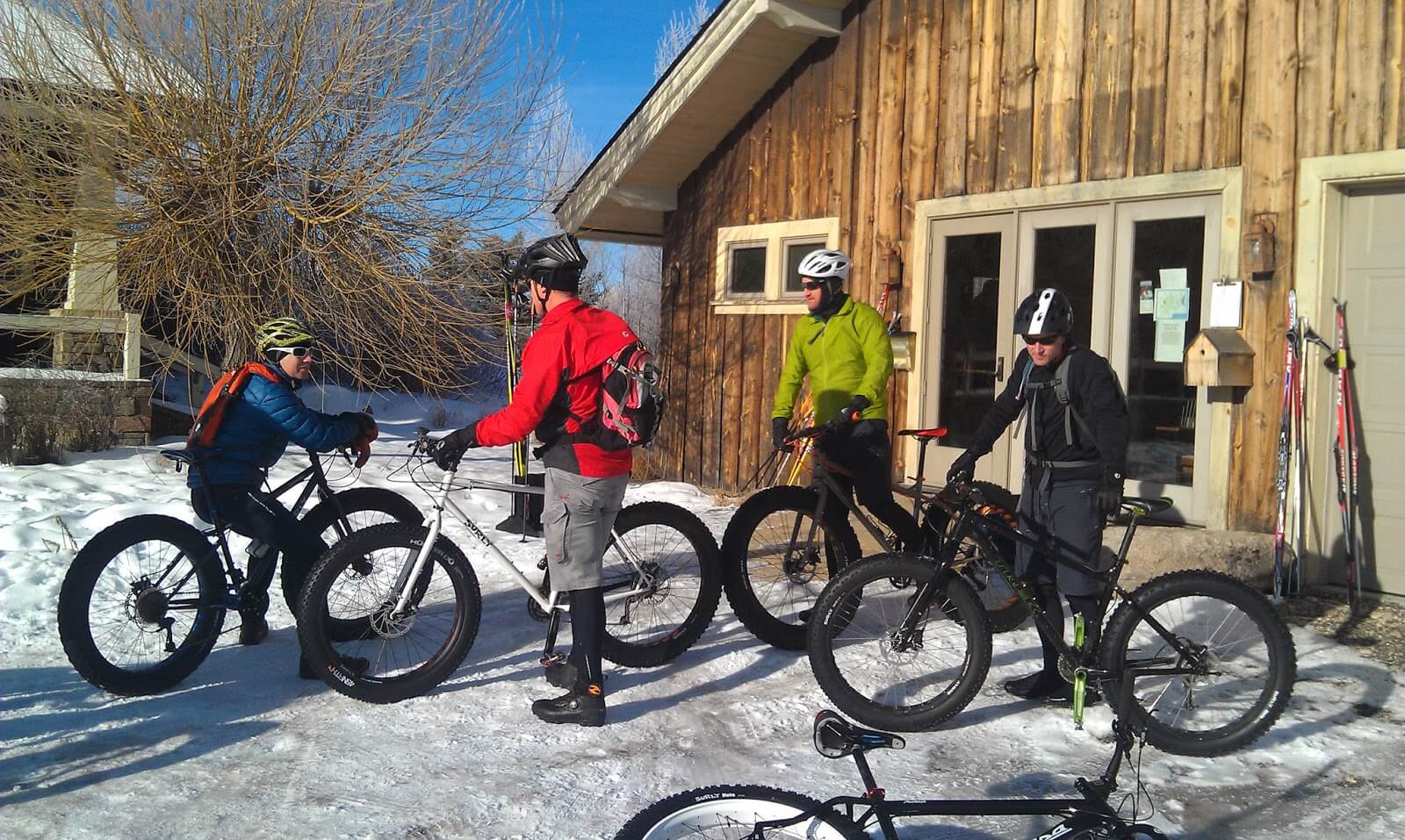 A group of four people with fat bikes outside a wooden building at Jug Mountain Ranch.