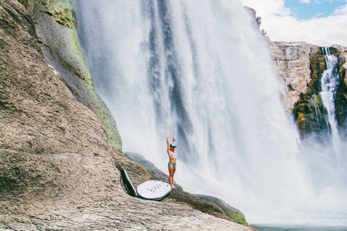 A woman standing near the base of a waterfall.