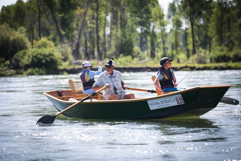 A man and his two grandsons sit in a row boat and cast ines into the South Fork of the Snake River.