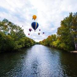 Air balloons floating over a river surrounded by trees.