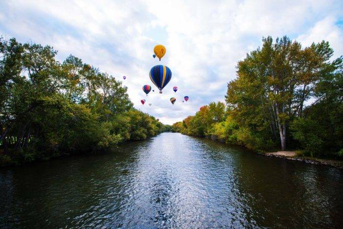 Air balloons floating over a river surrounded by trees.