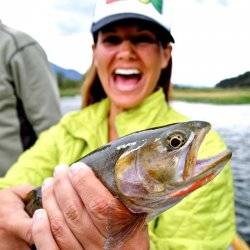 A woman in a neon green jacket smiles while holding a cutthroat trout.