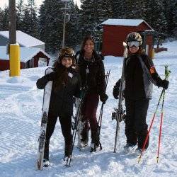 Three people in snow gear stand with ski equipment at Cottonwood Ski Resort.