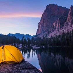 A lit up tent next to a large mountain as the sun sets.