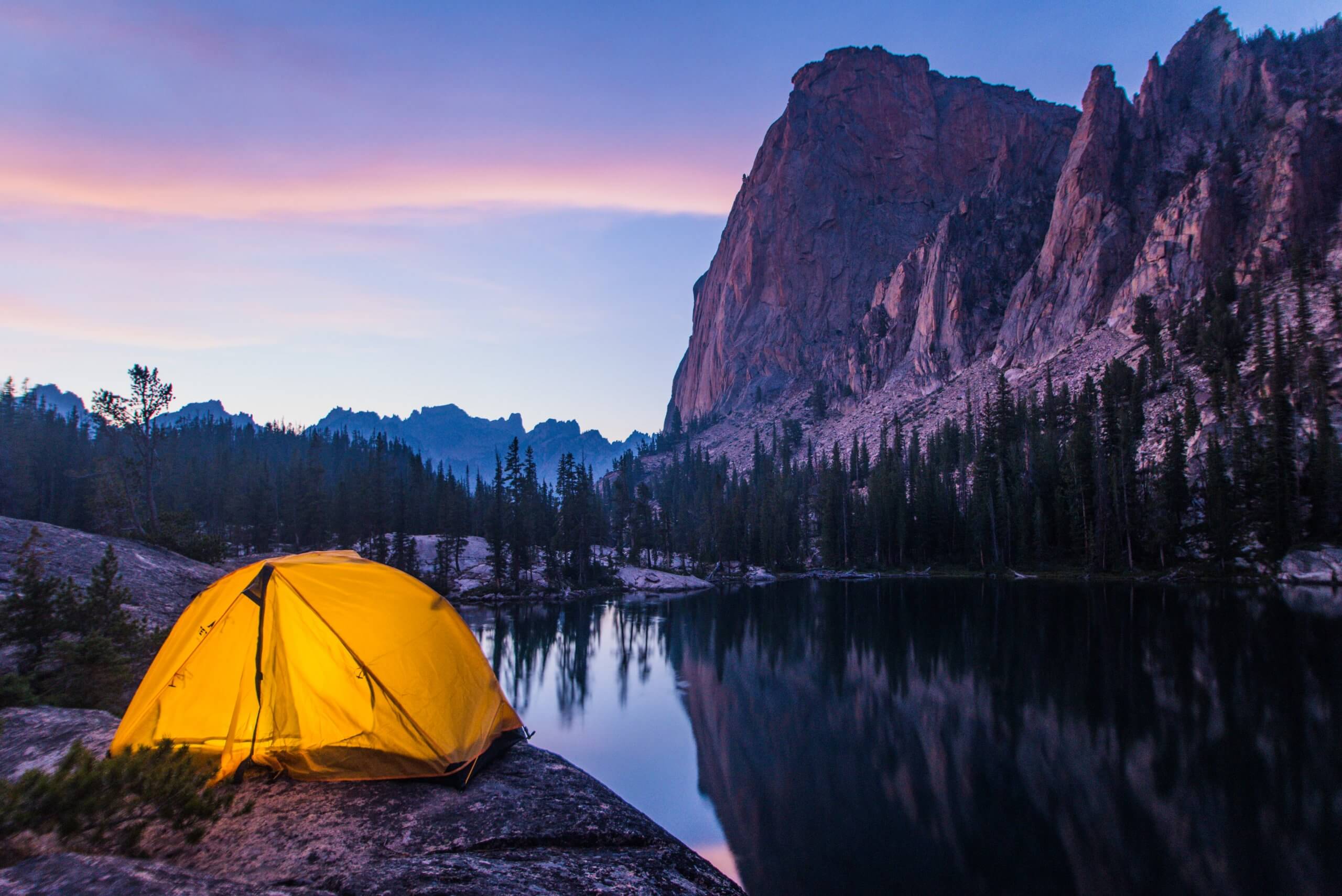 A lit up tent next to a large mountain as the sun sets.