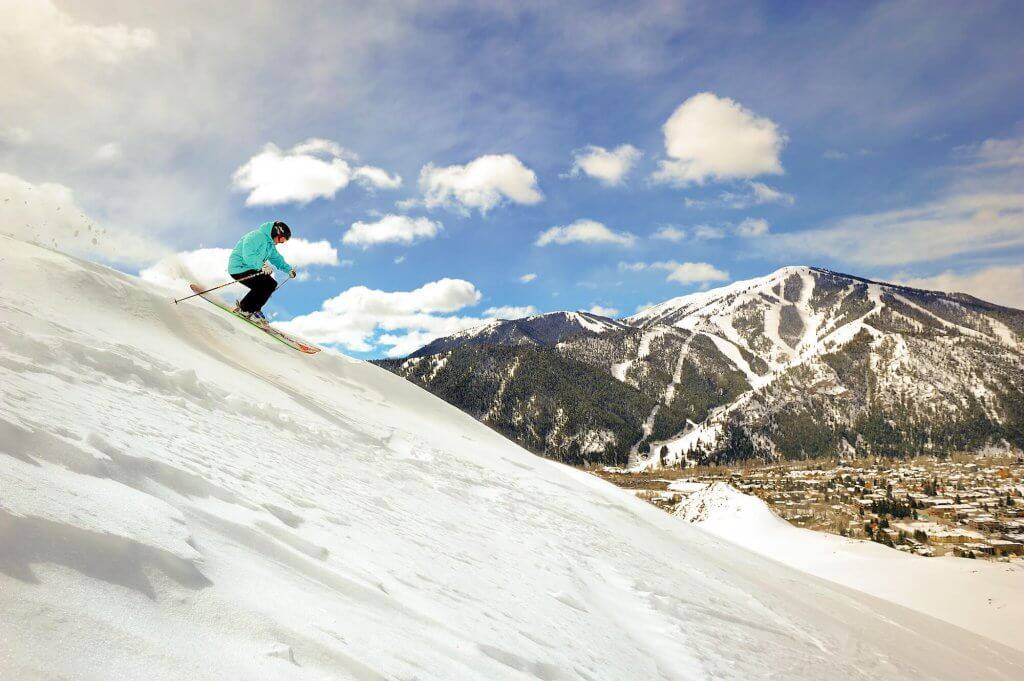 A person in a blue jacket skiing down a slope at Sun Valley Resort.