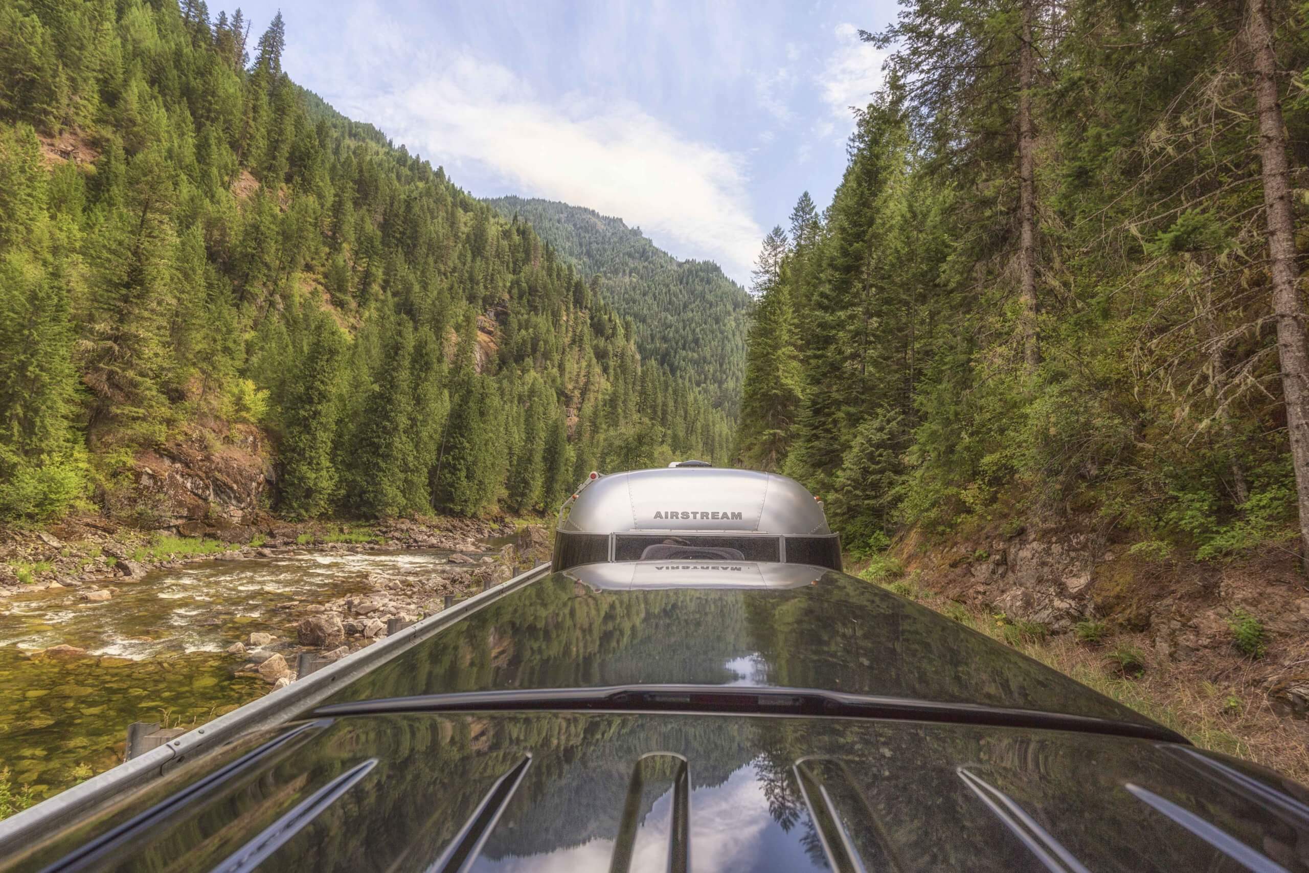 View from atop an Airstream trailer of the road, surrounded by trees and a river on the left.