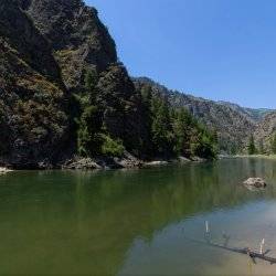 A panoramic snapshot of the still waters shining down the Main Salmon River where rugged landscape lines both sides.