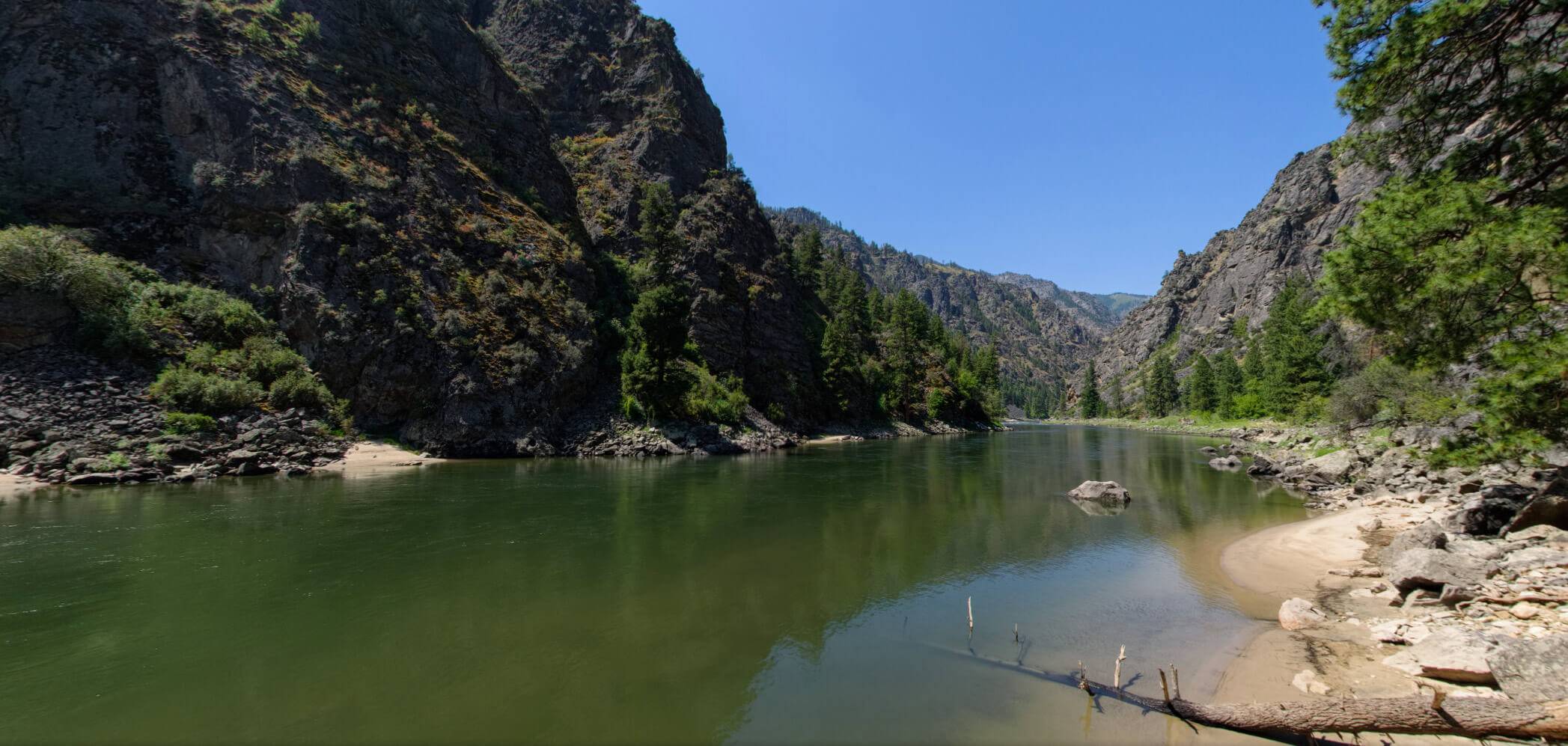 A panoramic snapshot of the still waters shining down the Main Salmon River where rugged landscape lines both sides.