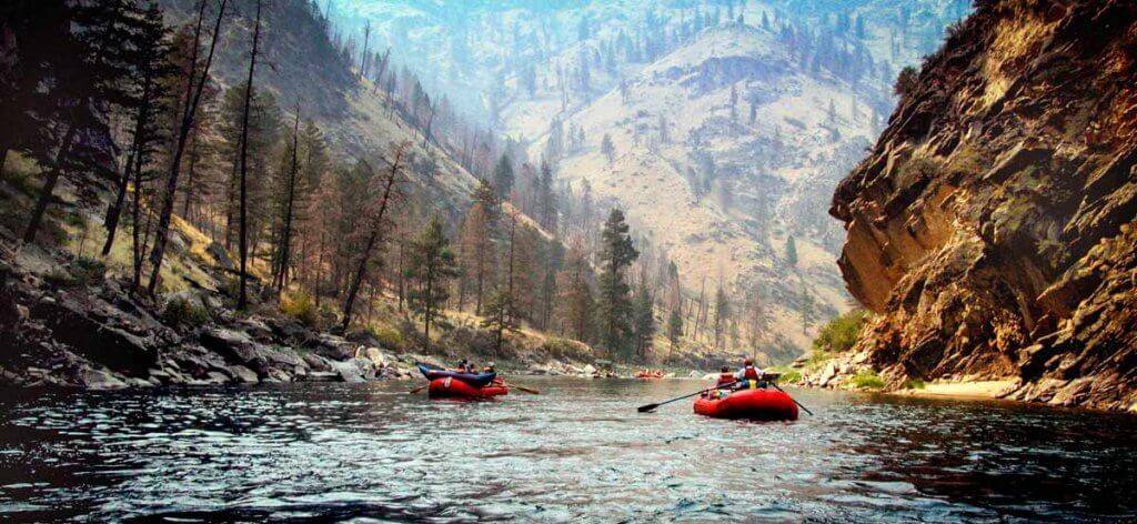 Red rafts headed down the Middle Fork of the Salmon River in Idaho as rugged mountains rise in the distance.