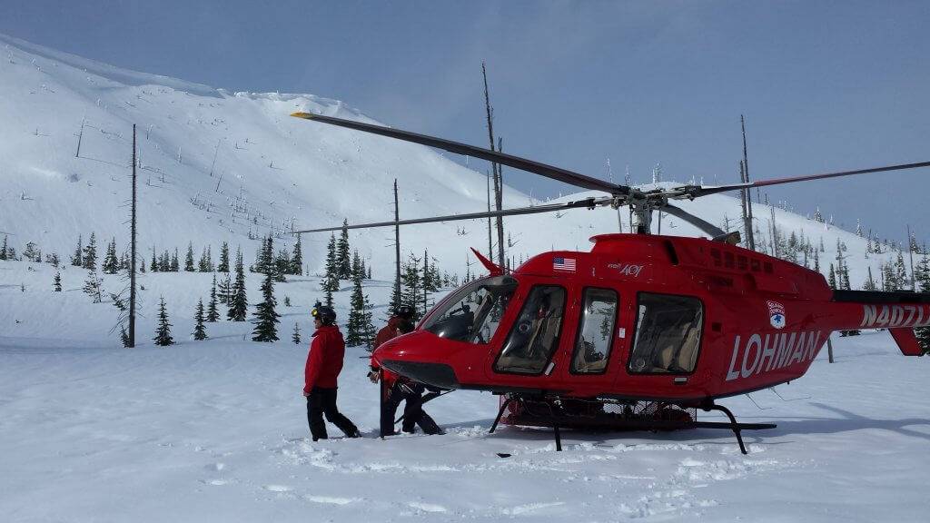 Skiers prepare to board a red helicopter for a heli ski outing.
