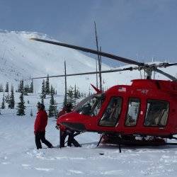 Skiers prepare to board a red helicopter for a heli ski outing.