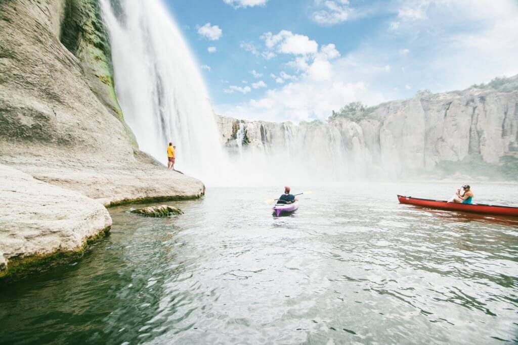 Two kayakers paddling beneath a waterfall.