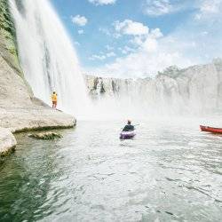 Two kayakers paddling beneath a waterfall.