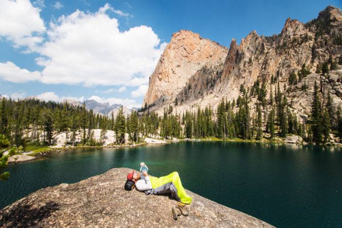 A man reading a book at next to a lake.