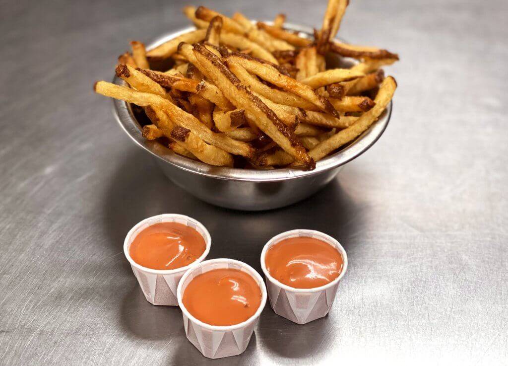 Three paper cups of fry sauce in front of french fries in a metal bowl.