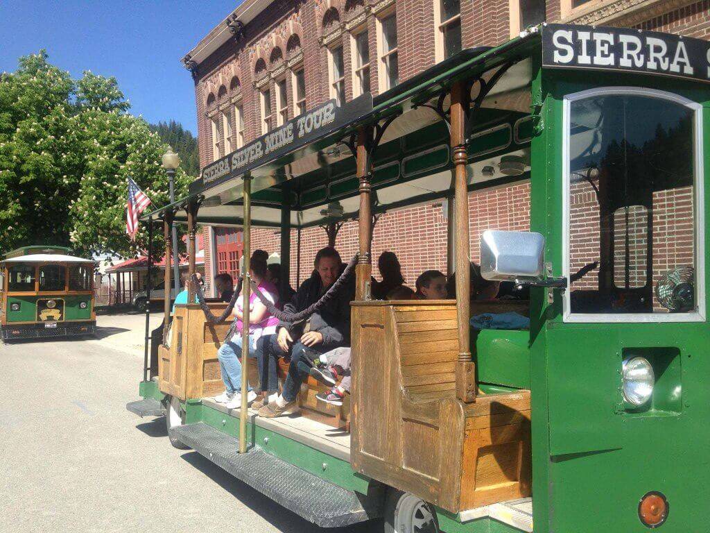 A group of people riding a trolley past a brick building on the Sierra Silver Mine Tour.