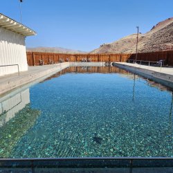 An empty natural rectangular hot pool filled with turquoise water that allows you to see the gravel bottom of the pool at Challis Hot Springs.