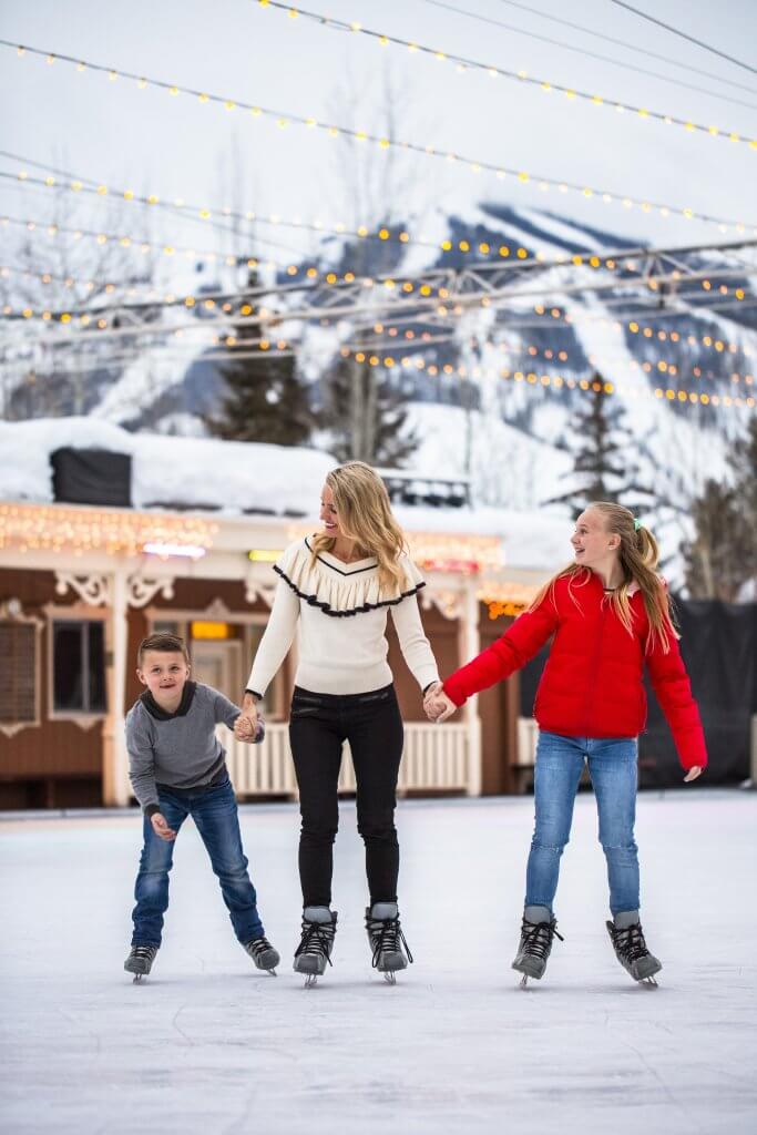 A woman and her two kids smile while ice skating at Sun Valley's Outdoor Ice Rink.