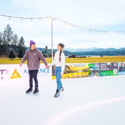 A couple join hands, laughing while ice skating outdoors at CDA On Ice at McEuen Park.