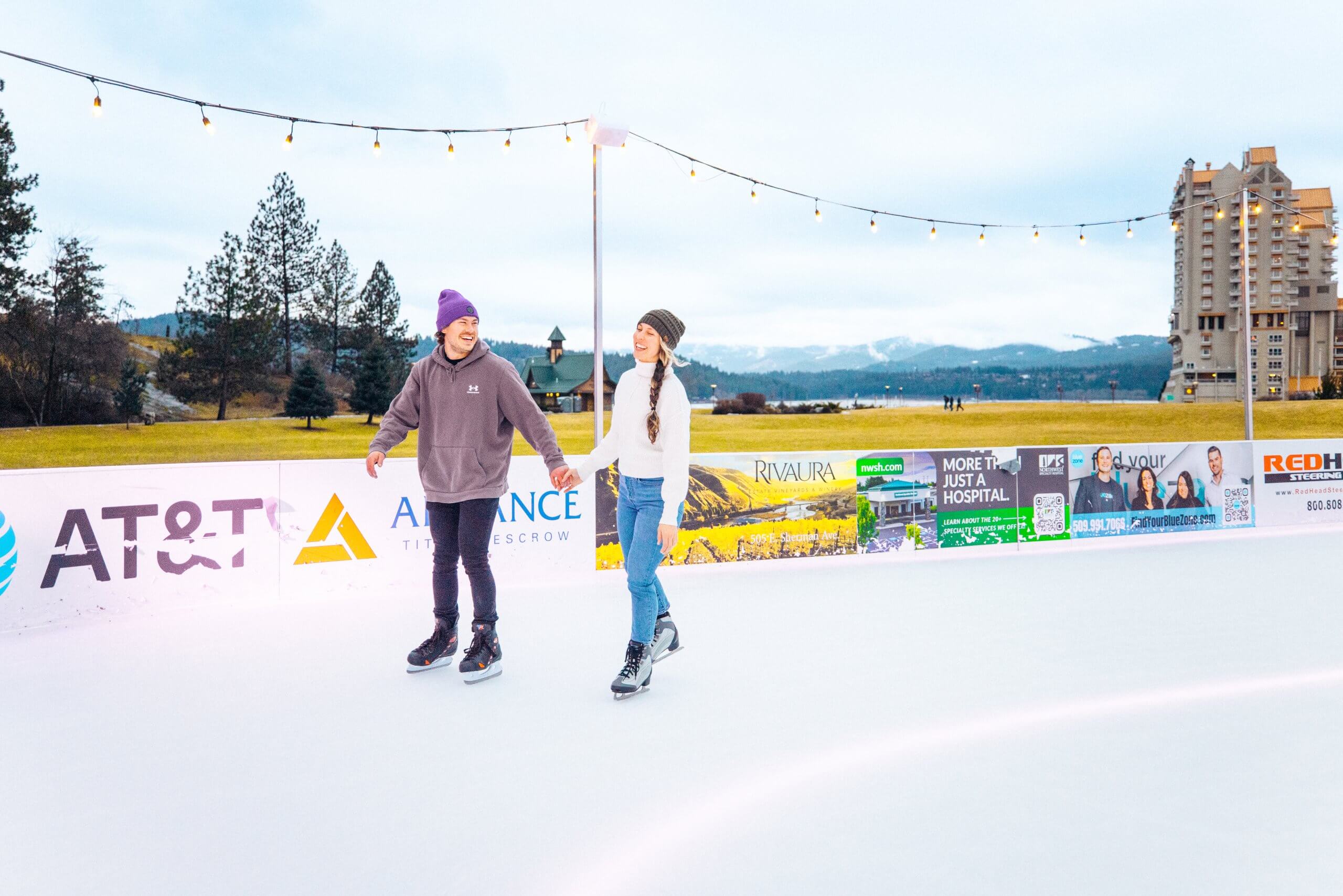 A couple join hands, laughing while ice skating outdoors at CDA On Ice at McEuen Park.