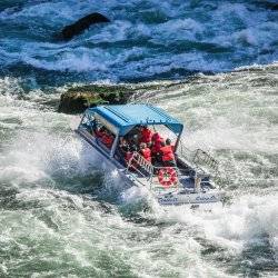 A jet boat cruises down a river, surrounded by white water