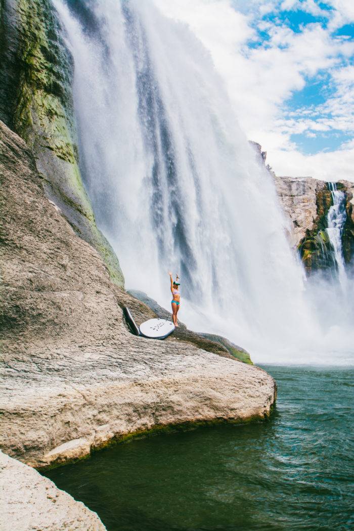 A woman standing beneath a towering waterfall.