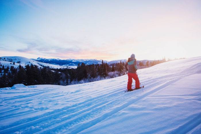 The sun rising as a hiker climbs a mountain in the snow.