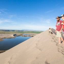 Two people standing on the top of a sand dune.